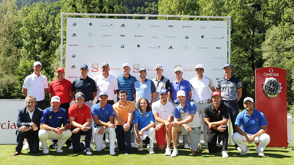 A group of the best golfers of the world in casual attire pose outdoors on a sunny day, with a sponsor backdrop and a red clock display behind them, conveying teamwork and sportsmanship.