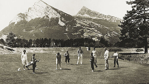Ein Bild in schwarz und weiss. Sechs Personen stehen auf dem Green und im Hintergrund sind die Berge zu sehen.